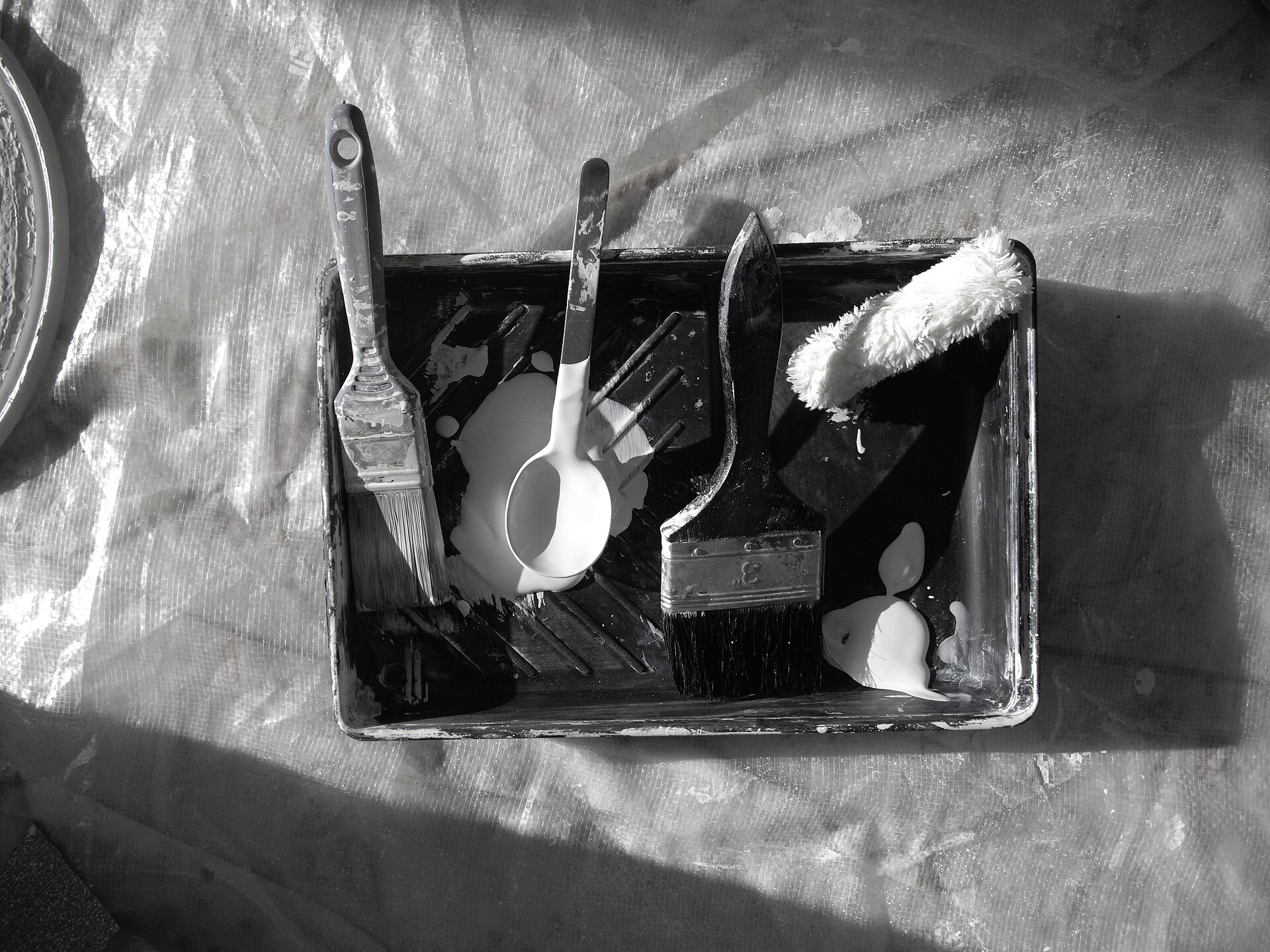 A paint tray with brushes and a roller, ready before any paint goes on the wall